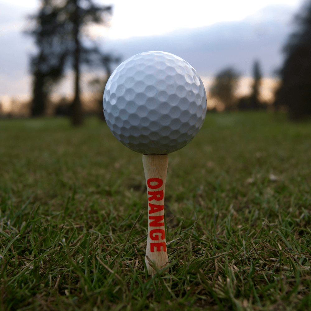 golf ball on top of orange bamboo golf tee on golf course