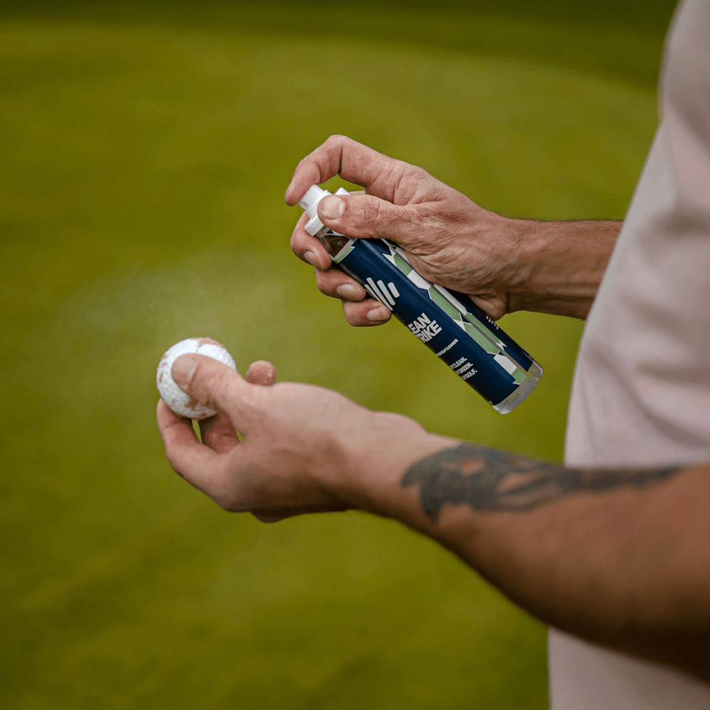 person spraying golf cleaning spray on a golf ball
